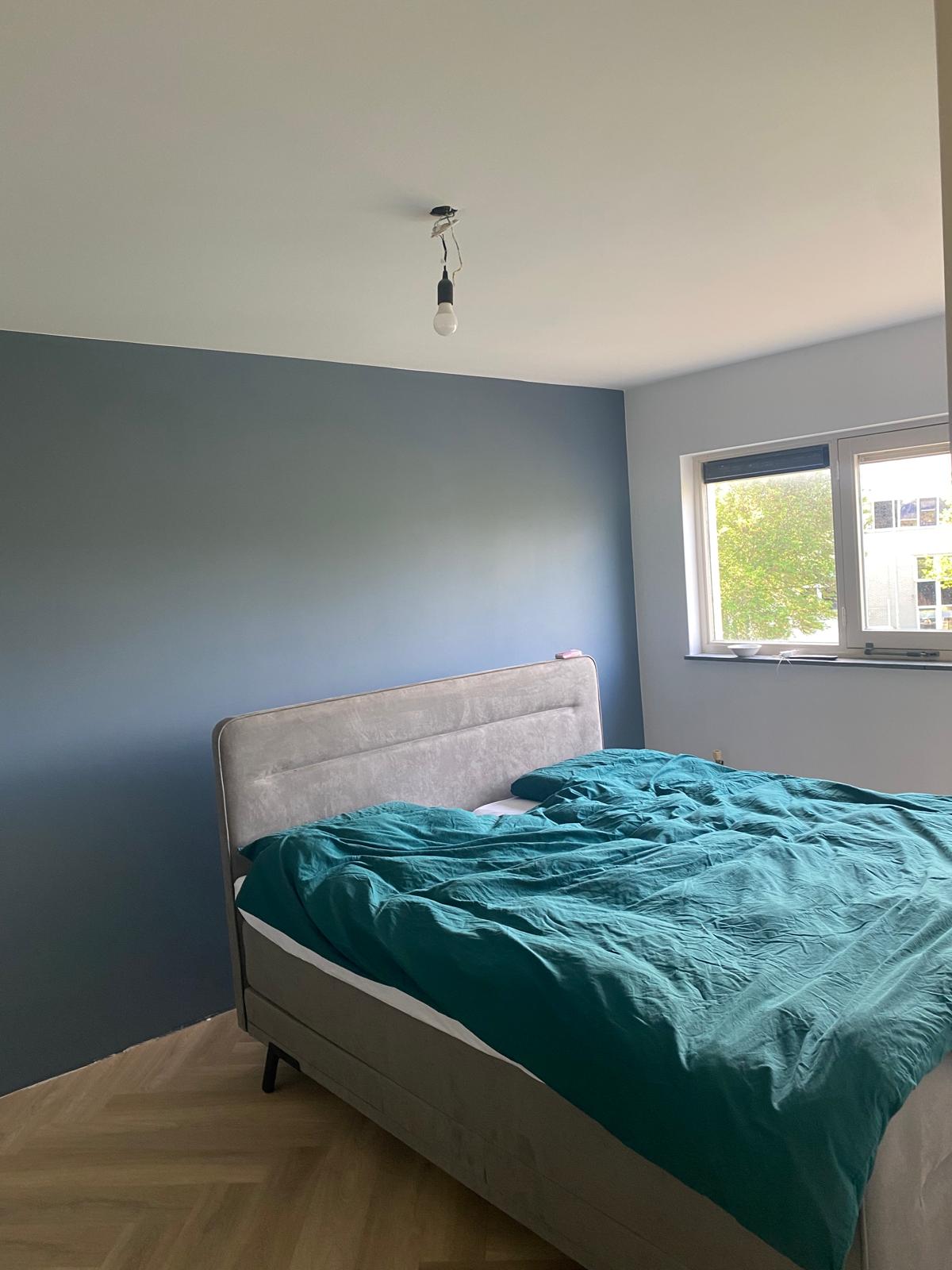 Slaapkamer met blauwgroene accentwand, strak afgewerkt