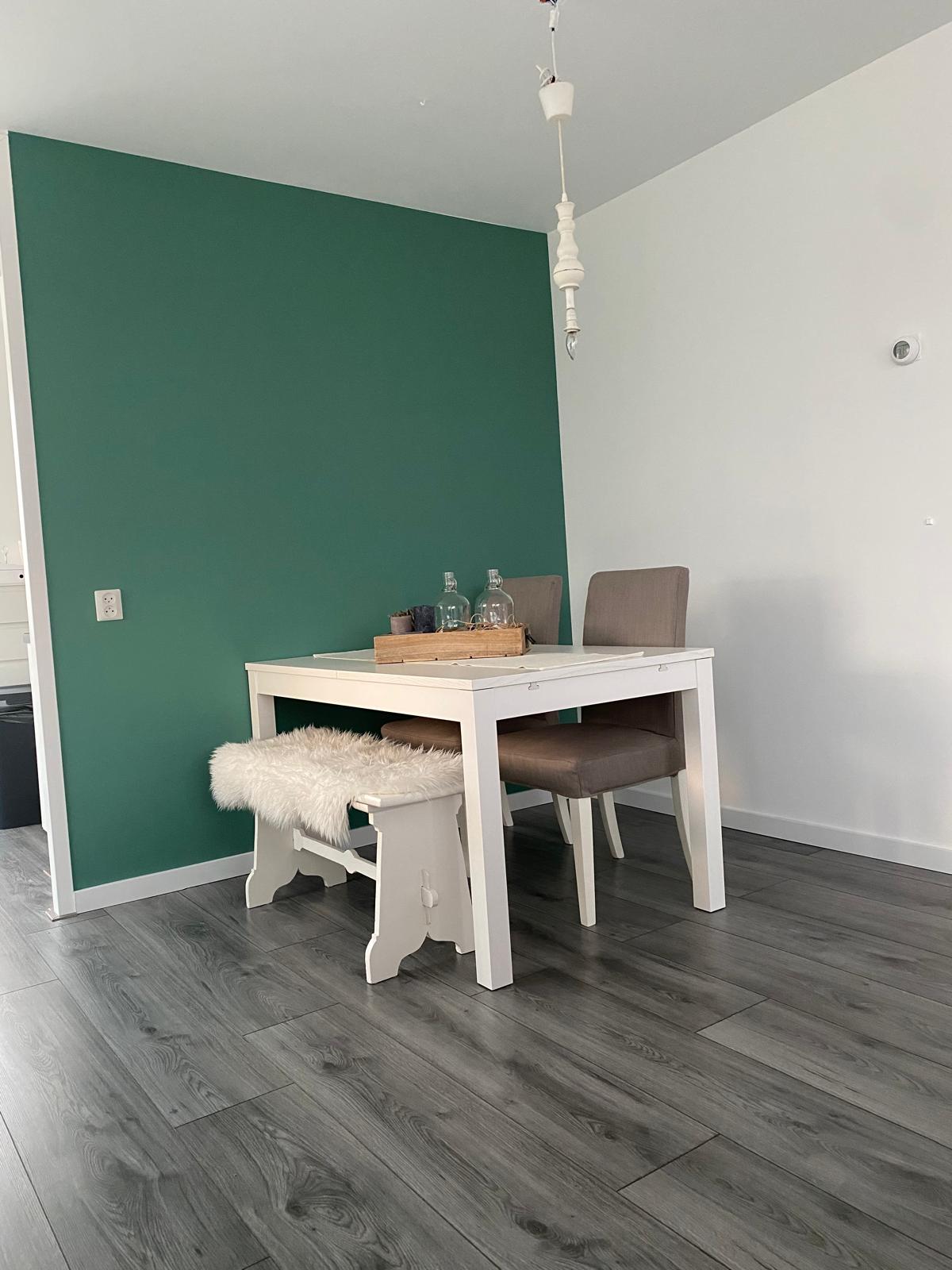 Eetkamer met groene accentwand en houten vloer